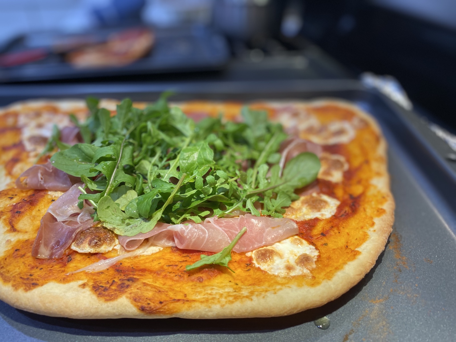 A finished flatbread pizza topped with arugula and prosciutto, fresh off the grill
